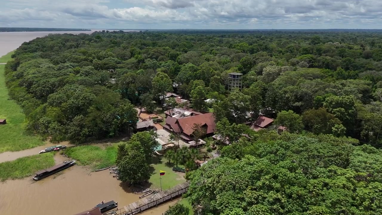 Cabanas rústicas cercadas por densa floresta amazônica perto de um rio sinuoso. Ideal para documentários de natureza ou conteúdo de viagem.