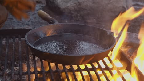 hot oil is poured from large cast iron skillet into campfire flames