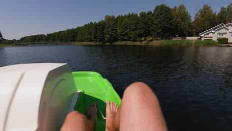 a relaxing view from a pedal boat on a calm lake, with feet visible in the foreground and a tree-lined shore in the distance