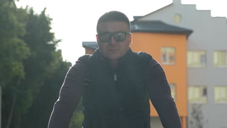 vista frontal de un hombre en bicicleta con gafas y mochila viajando por la ciudad. un hombre en una bicicleta de montaña viaja por el bosque y la ciudad al amanecer del verano.