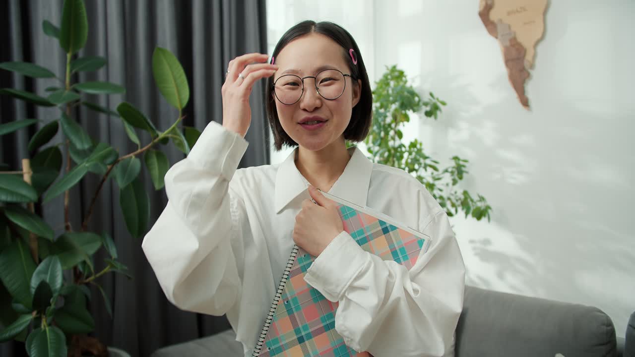 아름다운 아시아 여성의 초상화 카메라를 쳐다보며 매력적으로 미소를 지으며 노트북을 들고 있습니다.