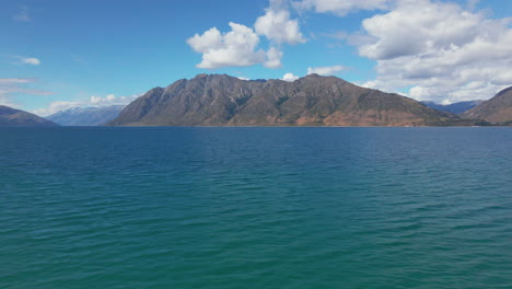 stunning blue water in lake hawea in new zealand and wild steep hills in the background