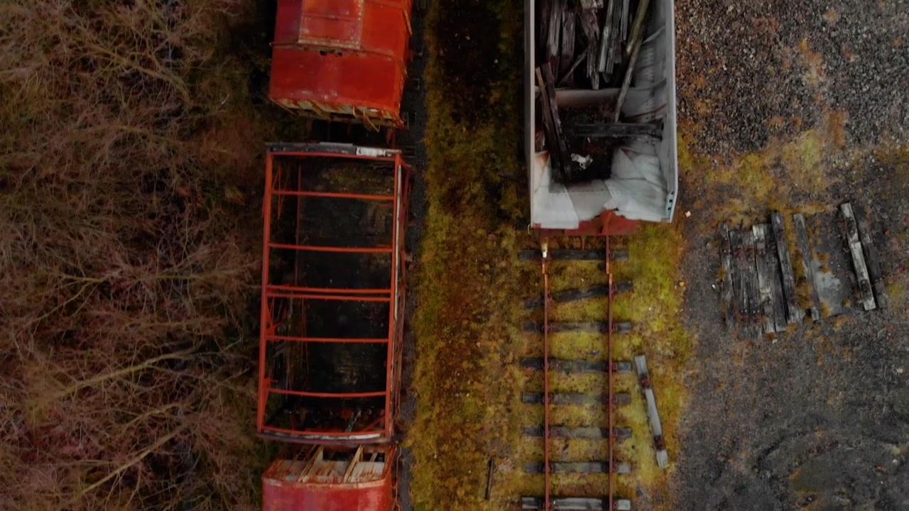 Fugleperspektiv droneoptagelser, der kigger lige ned på forladte, stærkt rustne røde togvogne, der står på forfaldne smalsporede spor ved det historiske Dunaskin industriarvsted i Ayrshire.