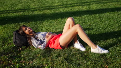 beautiful young hispanic woman resting and daydreaming in a grass public park field as she watches the clouds