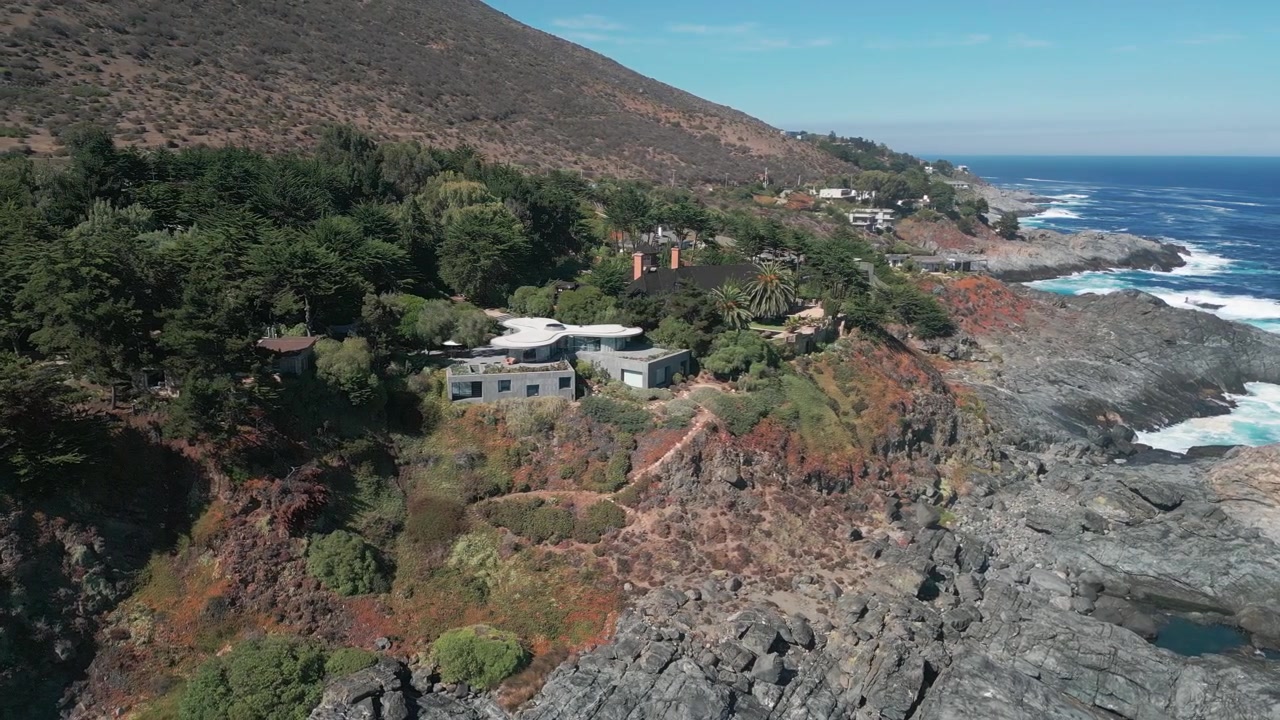 Dramatik kayalık kıyı şeridinin ve çarpan okyanus dalgalarının üzerinde, yerel bitki örtüsüyle engebeli bir uçurumun tepesine entegre edilmiş modern villaların üzerinde dairesel uçuş.