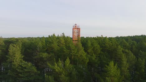 Vista-Aérea-Del-Faro-De-Bernati-Rodeado-De-Un-Exuberante-Bosque-De-Pinos-Verdes-Con-Nieve-Ligera,-Bosque-Nórdico,-Costa-Del-Mar-Báltico,-Soleado-Día-De-Invierno,-Letonia,-Amplio-Tiro-De-Drones-Avanzando-Sobre-Las-Copas-De-Los-árboles