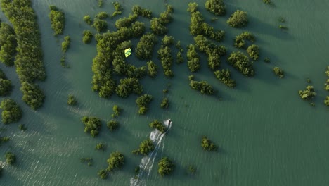 Wide-aerial-shot-of-a-kitesurfer-racing-through-mangrove-forest-on-a-windy-day,-and-the-sun-low-on-the-horizon-on-the-coast-of-Northern-Brazil