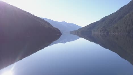 Spectral-sun-reflects-off-deep-blue-mountain-lake-in-ethereal-aerial