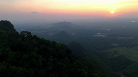 aerial above scenic sunset landscape, orange horizon in green foggy countryside of surat thani, thailand.