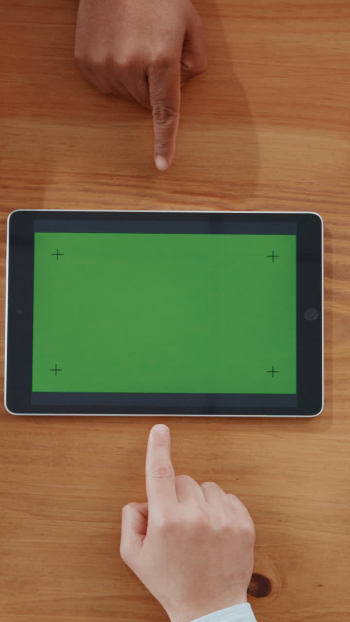 Two People Pointing at Green Screen Tablet on Wooden Table