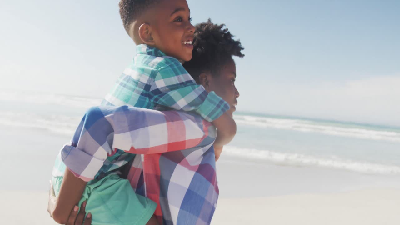 Afrikansk-amerikansk mor giver sin søn en tur på ryggen på stranden