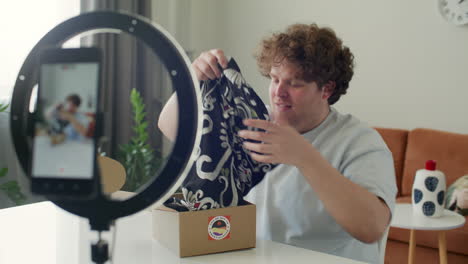 male blogger recording clothing unboxing video with phone at home