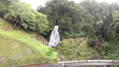 Waterfall-by-roadside-in-Ribeira-dos-Caldeirões-natural-park-near-Achada,-Azores,-Portugal---Low-angle-revealing-aerial-shot