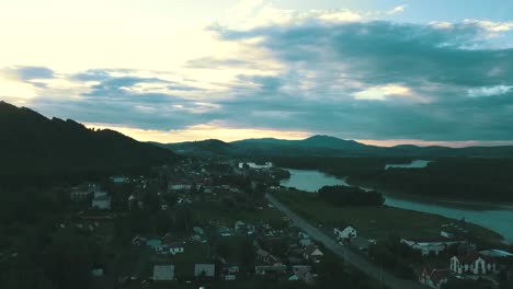 Luftaufnahme-Einer-Touristenstadt-In-Den-Bergen-Unter-Den-Wolken-Bei-Sonnenuntergang-In-Der-Nähe-Des-Gebirgsflusses