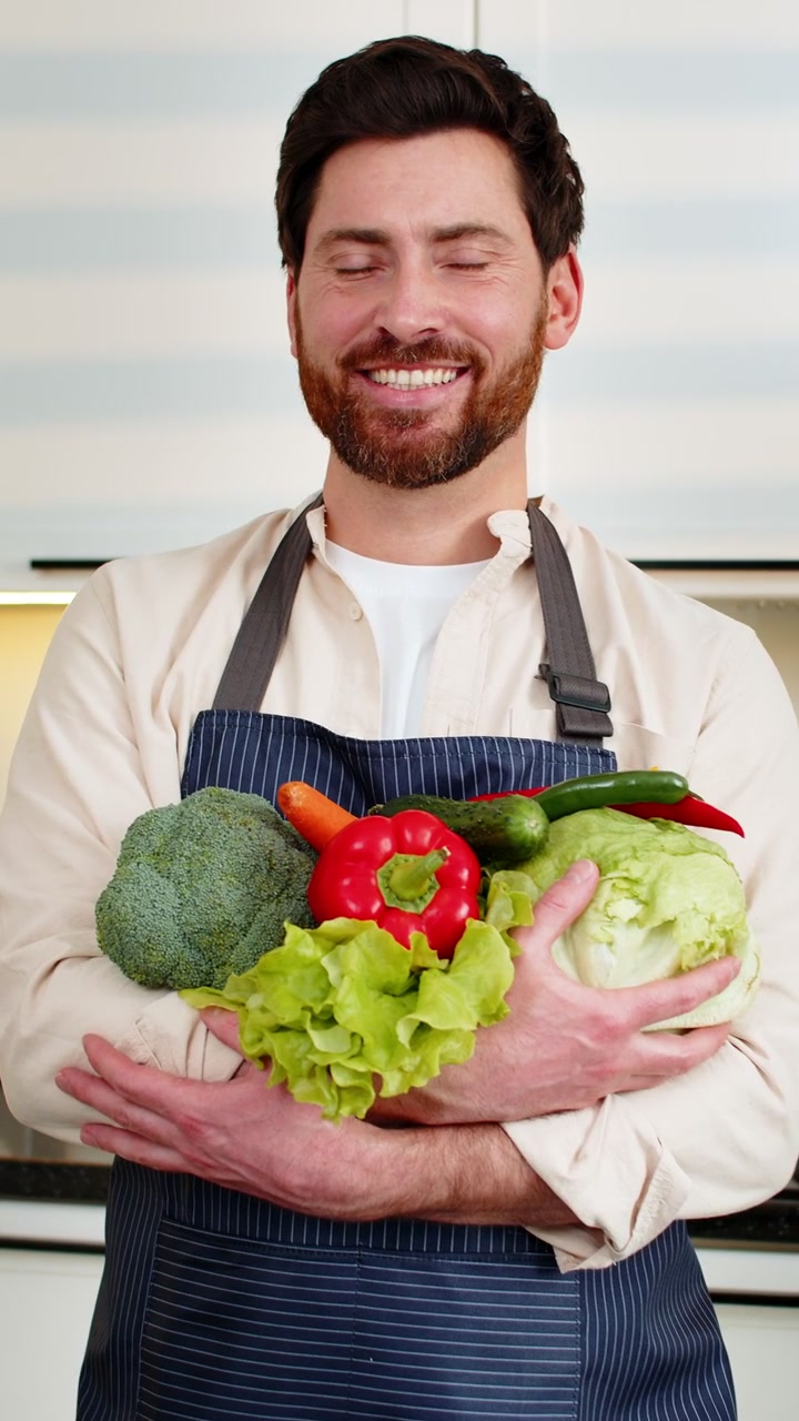 Uomo di mezza età che tiene in mano verdure fresche nella cucina di casa, sorridente per la preparazione di un pasto salutare