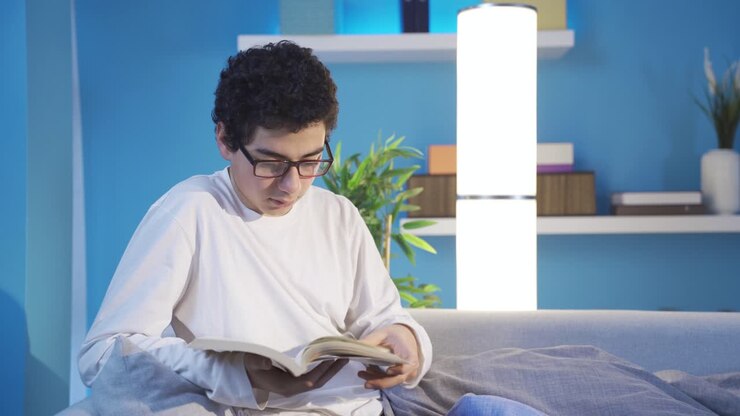 Handsome boy reading a book at home, daydreaming, diving into a book.