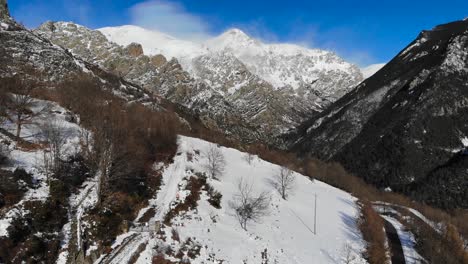 Aerial:-snowy-mountain-slope-with-snow-covered-mountains-in-the-background