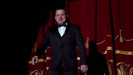 portrait of a host. man actor in black costume appears on stage and begins the speech in bright light spot in the theater.