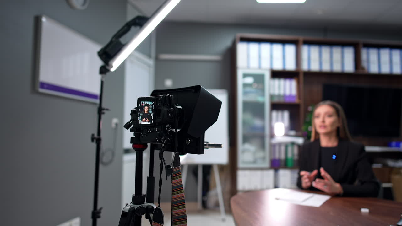 Blog footage in the office. Female influencer speaks to camera gesturing with her hands. Blurred backdrop.