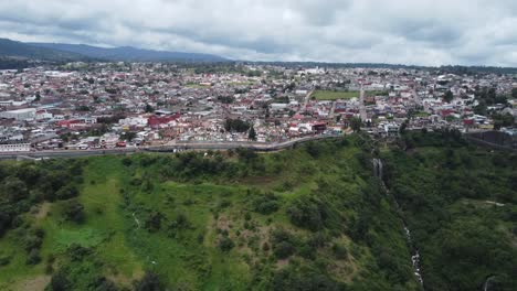 Historic-center-of-Zacatlan-filled-with-traditional-houses,-church-buildings,-and-public-gardens-through-clouds,-Atmospheric-cityscape,-Puebla,-Mexico,-Drone-shot