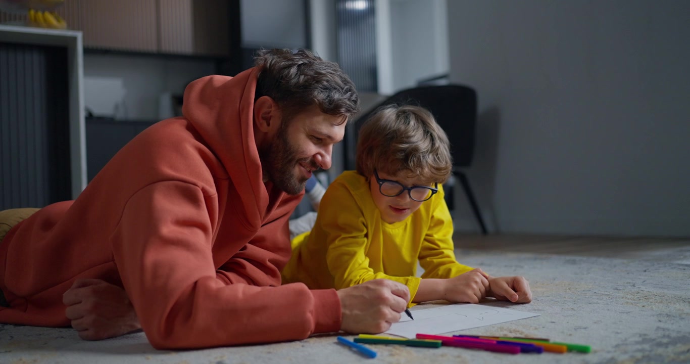 Padre e figlio felici che disegnano su carta a casa.