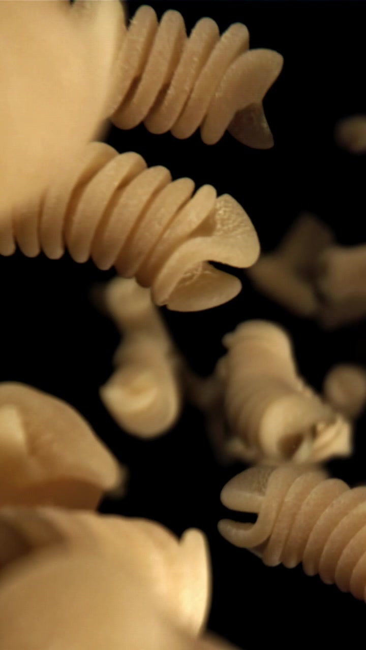 Pasta fusilli cruda che cade al rallentatore su sfondo nero