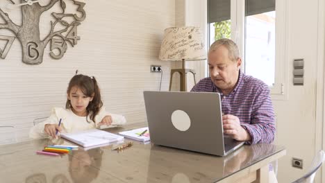 girl coloring with her grandpa while working on a laptop at home