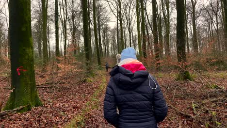 Toma-De-Seguimiento-En-Cámara-Lenta-De-Una-Mujer-Vestida-Con-Ropa-De-Invierno-Caminando-Al-Aire-Libre-En-Un-Bosque-Colorido-Con-árboles-Altos