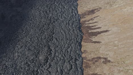 black solid lava field on slope of valley mountain in iceland, aerial