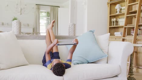 happy african american boy sitting on sofa and using tablet, in slow motion