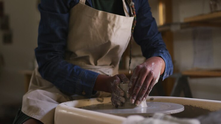 Mid section of female potter creating pottery on potters wheel at pottery studio