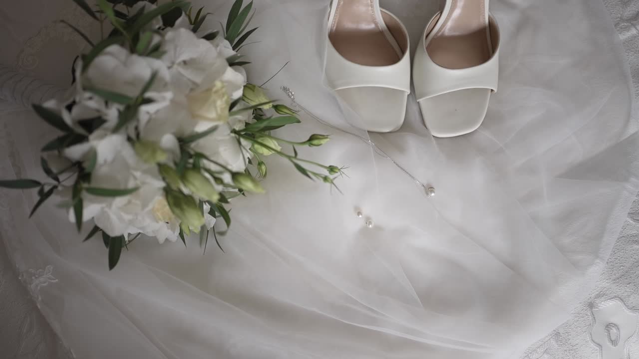 White bridal shoes, necklace, and fresh bouquet on satin