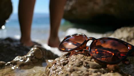 gafas de sol en la orilla de la playa, mujer nadando en el mar en el fondo