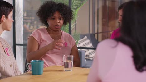 group of women wearing pink breast cancer awareness ribbons meeting and talking at therapy support group for cancer treatment patients 9