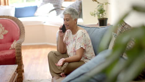 Happy-senior-biracial-woman-sitting-on-couch-and-talking-on-smartphone-at-home,-slow-motion