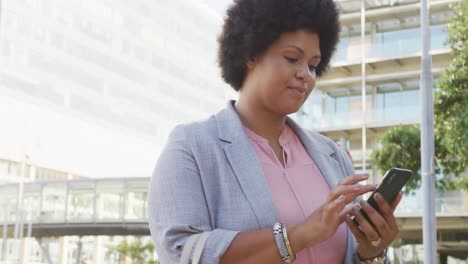 Portrait-of-happy-plus-size-biracial-woman-using-smartphone-in-city