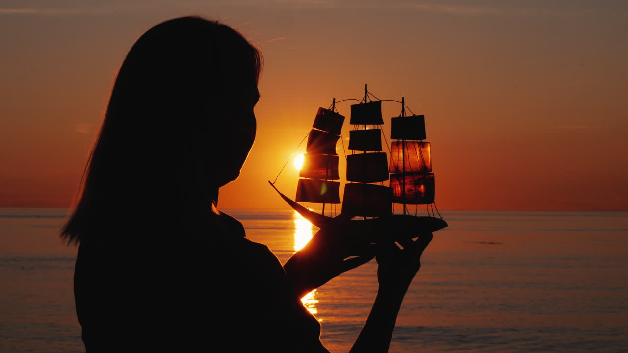 그녀의 손에 범선을 가진 여자의 실루엣 석양은 돛 영감을 통해 빛난다