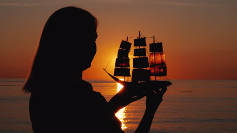 Silhouette-Of-A-Woman-With-A-Sailboat-In-Her-Hands-The-Setting-Sun-Shines-Through-The-Sails-Inspirat