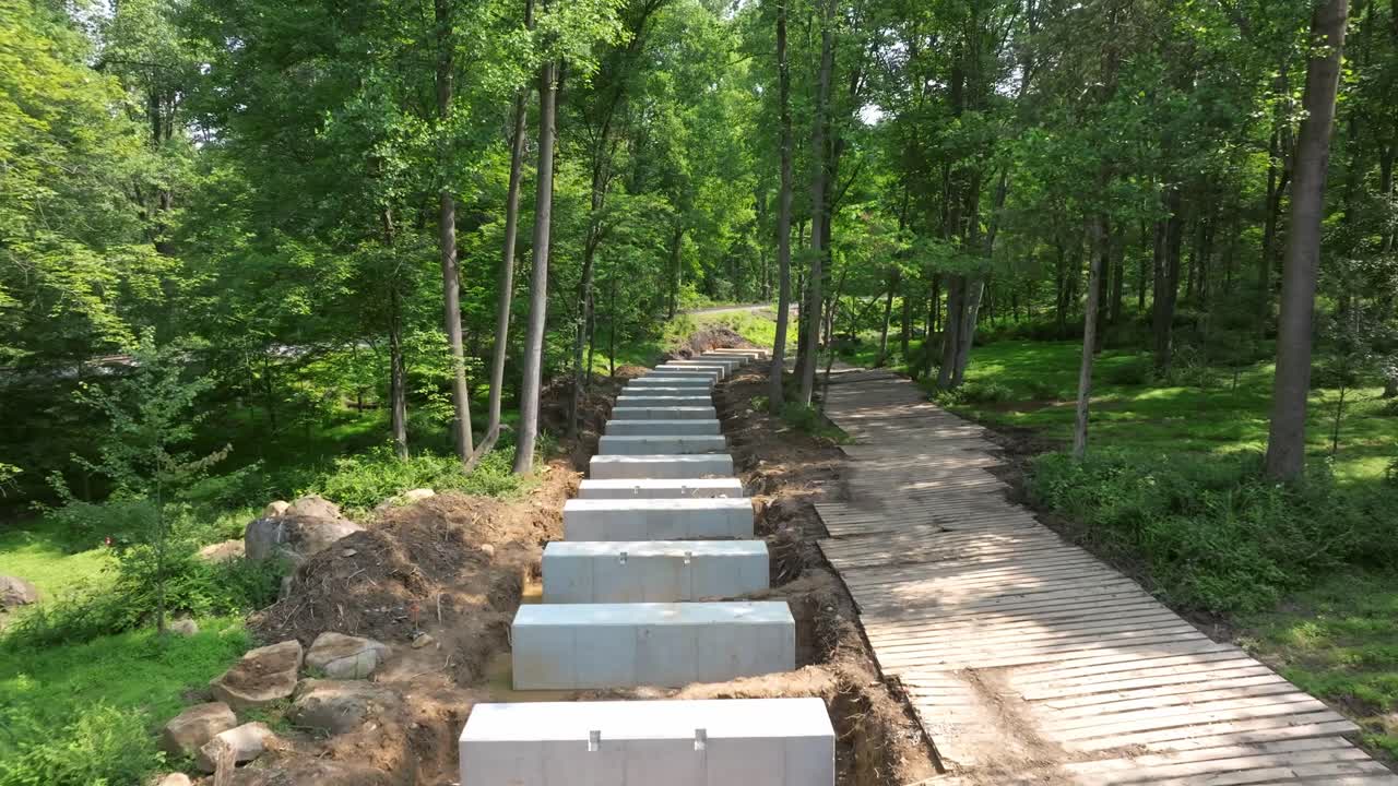 Workers are constructing a new surrounded by lush greenery. Concrete blocks are being placed to form the Rail Road Trestle, with a wooden walkway alongside