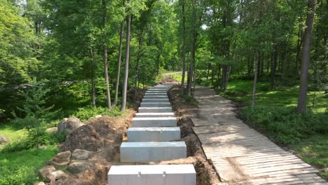 workers are constructing a new surrounded by lush greenery. concrete blocks are being placed to form the rail road trestle, with a wooden walkway alongside