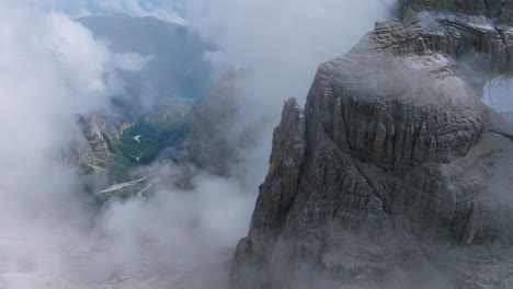 aerial flight through dense clouds revealing mountains and green valley in dolomites