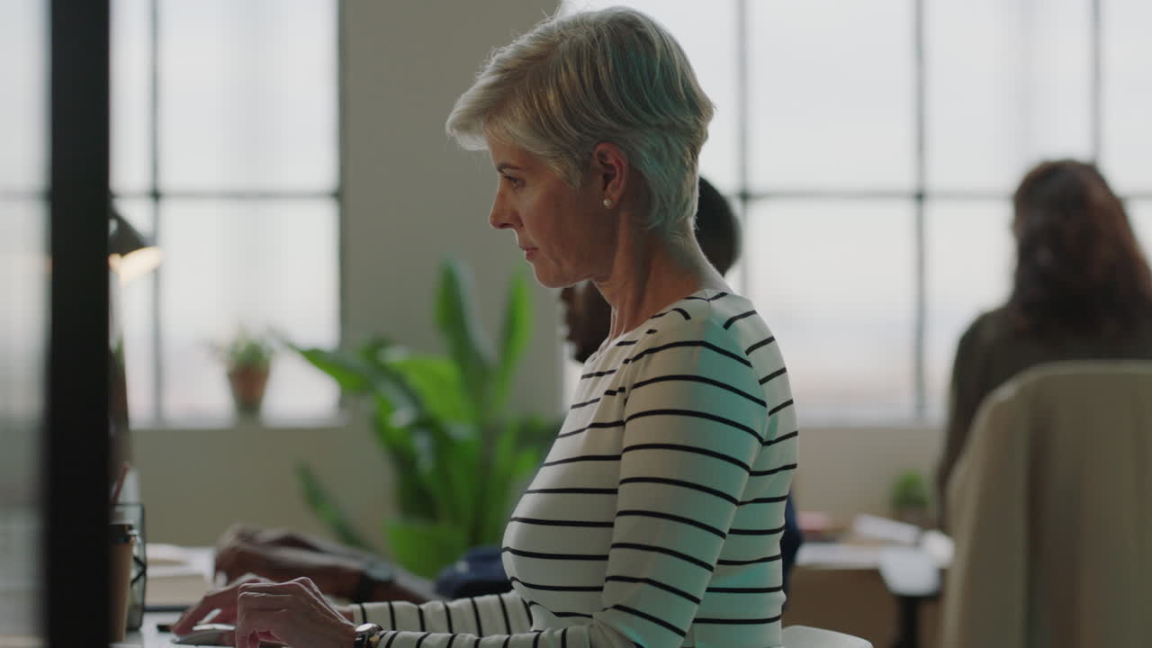 mature business woman typing using computer sending email networking diverse team in busy office workspace