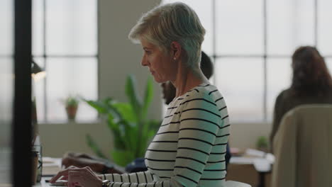 mujer de negocios madura escribiendo usando la computadora enviando correos electrónicos creando redes equipo diverso en el ocupado espacio de trabajo de la oficina