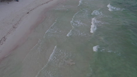 Aerial-Top-down-shot-of-rolling-waves-in-a-crystal-clear-blue-ocean-into-a-pristine-white-sand-beach-in-Cancun,-Mexico