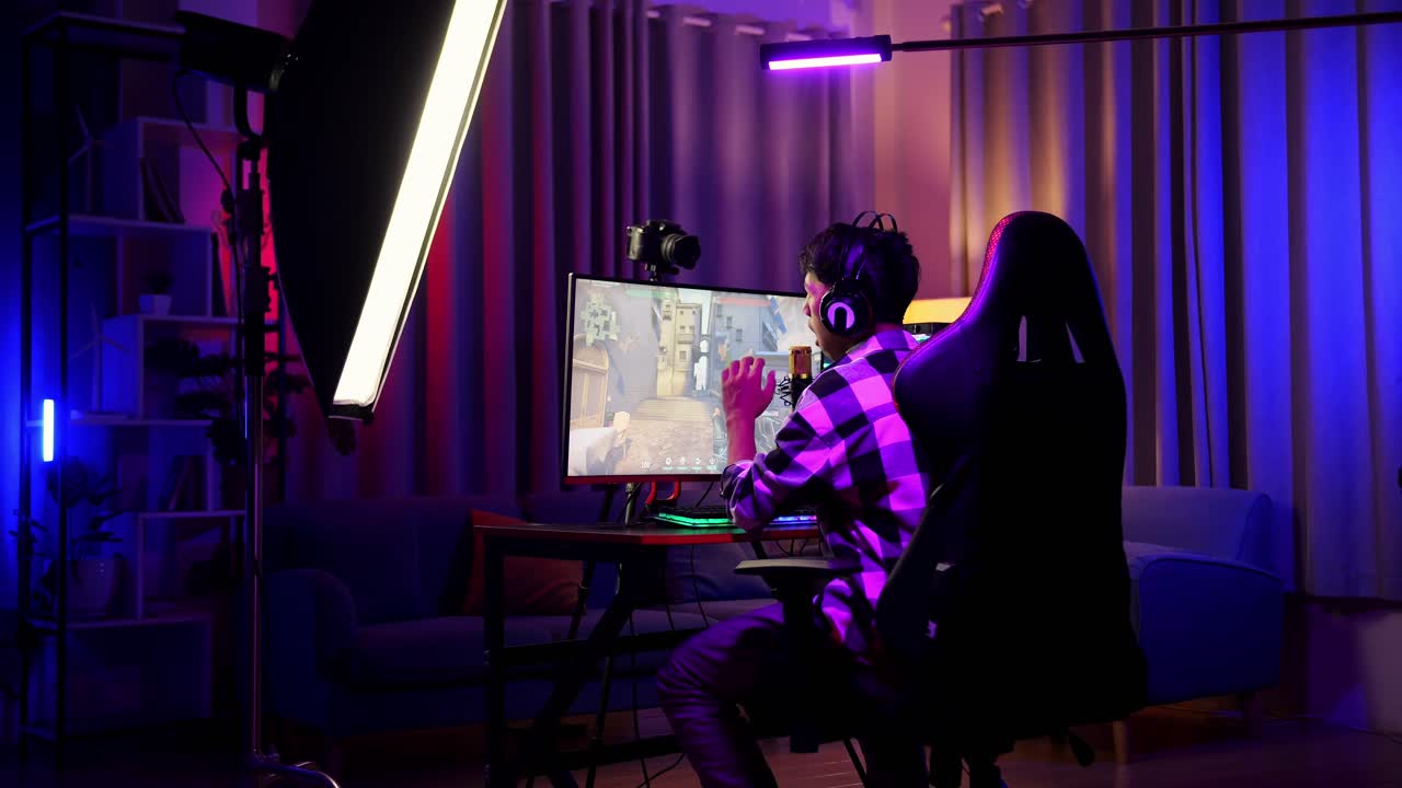 vista trasera de un chico asiático jugando a un juego en red en una computadora personal. bostezando y durmiendo, videojuego de transmisión en vivo, escritorio iluminado por luz de tira led rgb