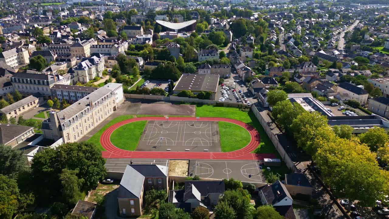 Drone aerial of Laval city with buildings, river, bridges under clear blue sky, approach to track and field area