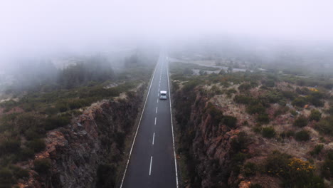 Mystische-Luftneigung-Nach-Unten-Zeigt-Autofahren-Auf-Asphaltierter-Landstraße-In-Nebel-Und-Wolken-Am-Morgen