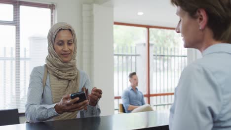 smiling biracial woman paying with credit card at reception at modern dental clinic
