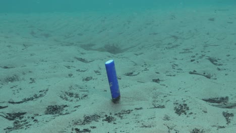 underwater footage of a discarded cigarette lighter bobbing along the sea floor in the ocean current