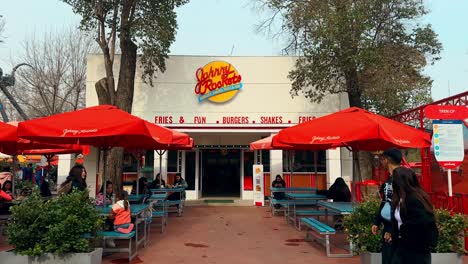 panoramic establishing of people walking past the johnny rockets thematic hamburger restaurant on a sunny day, santiago, chile. fantasilandia amusement park